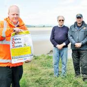 Mike Davis, training officer for Bay Search and Rescue, Queen’s Guide Cedric Robinson and Nigel Capstick, station officer for Arnside Coastguard, with a copy of The Westmorland Gazette Safety on the Sands poster